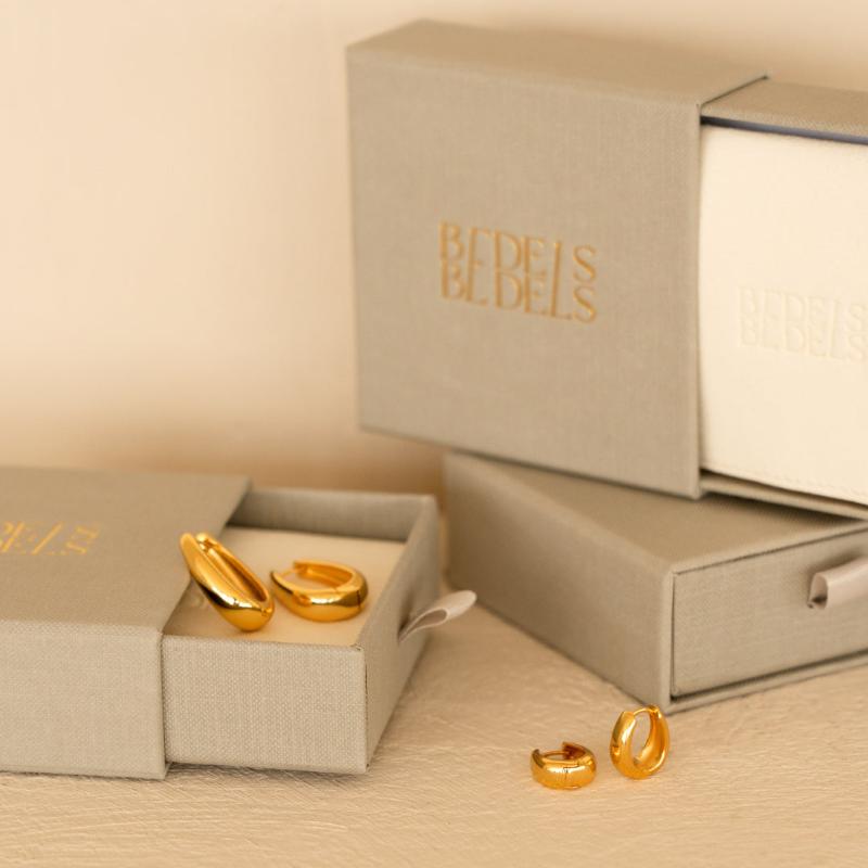 De AMARA en CELINA oorbellen in goud van Bedels & Bedels, gepresenteerd met luxe verpakking met het gouden logo en fluwelen pouch.