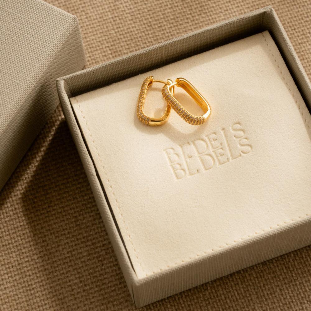 Statement oorbellen in rechthoekig design, goudkleurig en ingelegd met zirkonia, gepresenteerd in een luxe verpakking voor een elegante unboxing ervaring.
