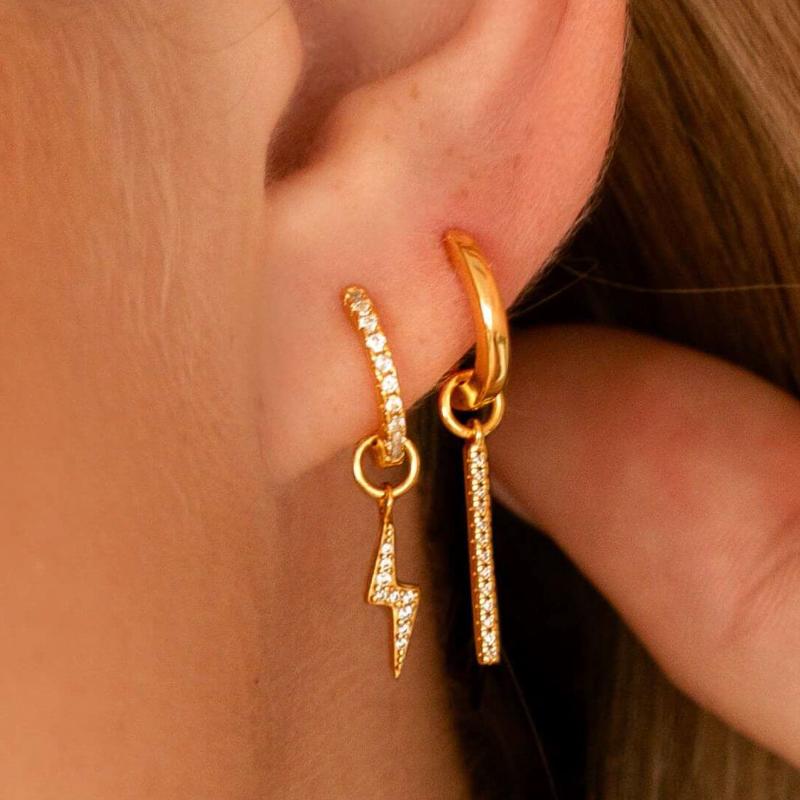 Huggies met bedels in de vorm van een bliksem en een staafje, goudkleurig en ingelegd met zirkonia.