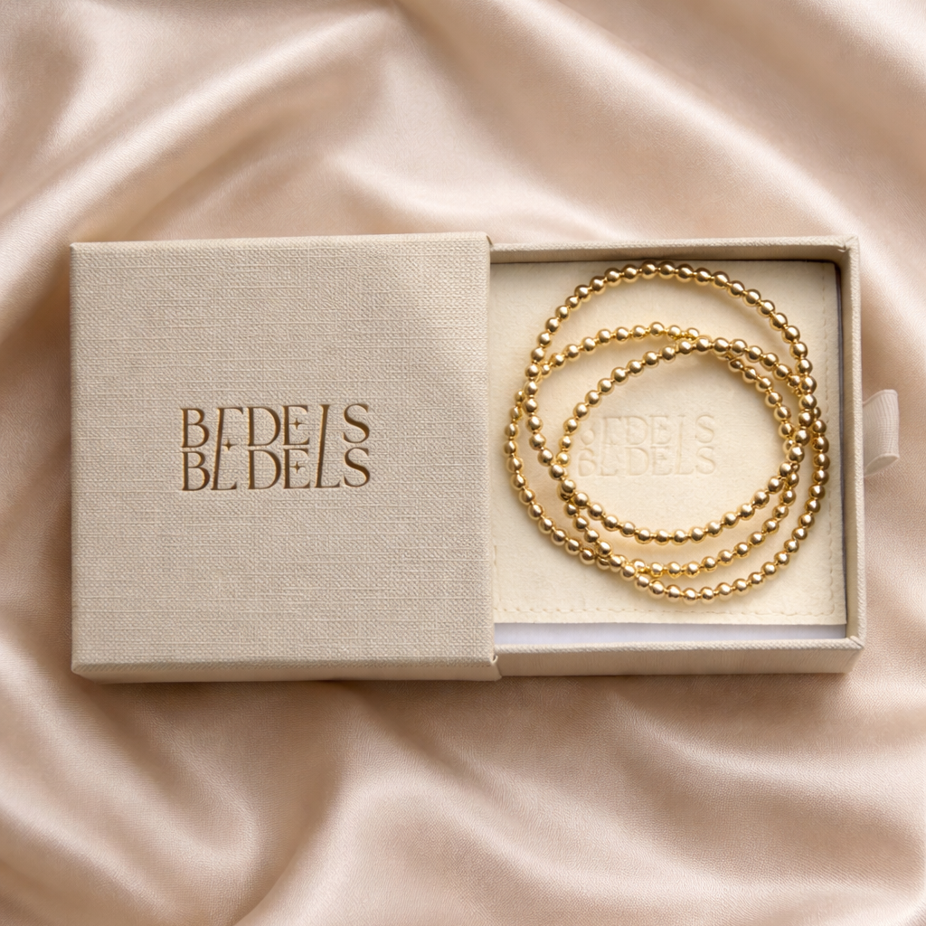 Gouden kralenarmbanden in geopend sieradendoosje met suède inlay op champagnekleurig satijn