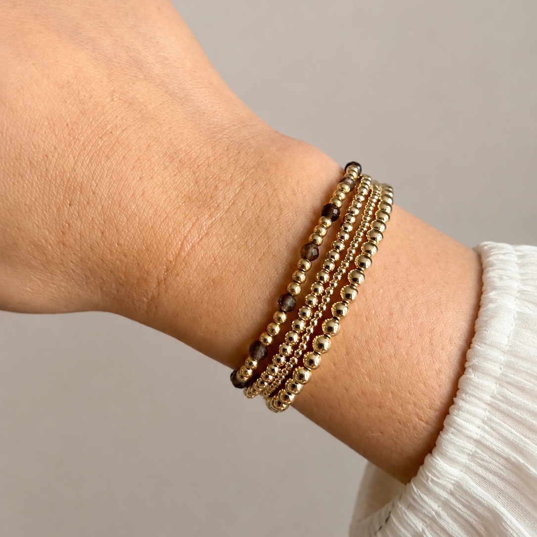 Vier gold filled kralenarmbanden om de pols bij witte blouse, waarvan één met rookkwarts kralen