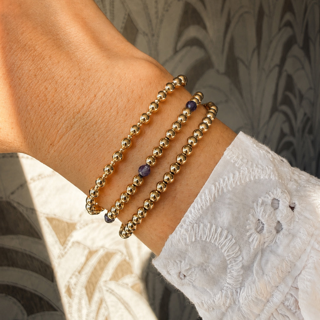 Pols van model met gestapelde gouden kralenarmbanden van gold filled 14K met iolite accenten, van Bedels & Bedels.