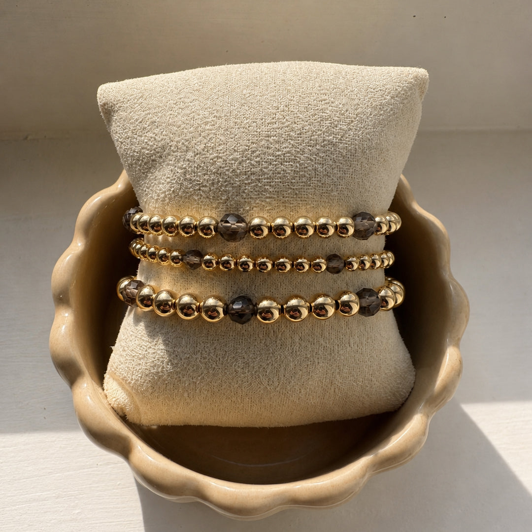 Gouden armbanden met heldere obsidiaan en rookkwarts edelstenen gecombineerd met gouden kralen, van Bedels & Bedels.