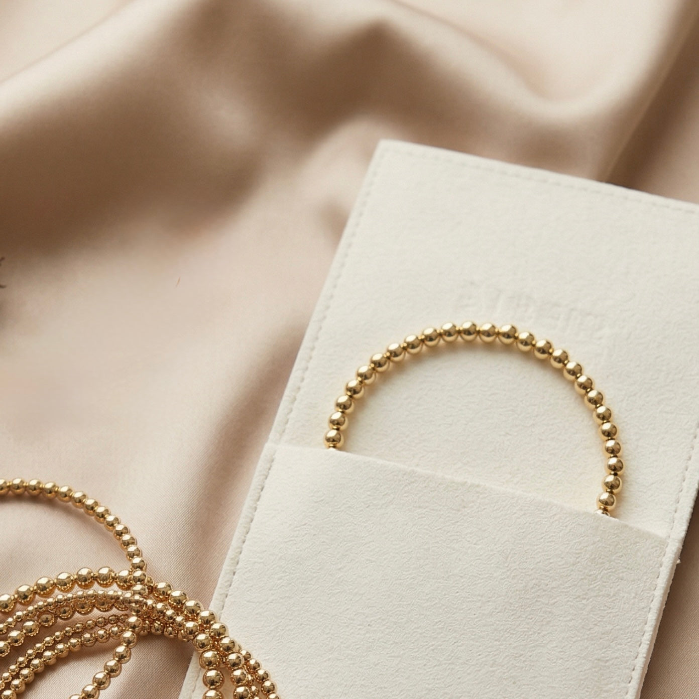 Close-up van gouden 4mm kralenarmband die uit een suède sieradenzakje steekt