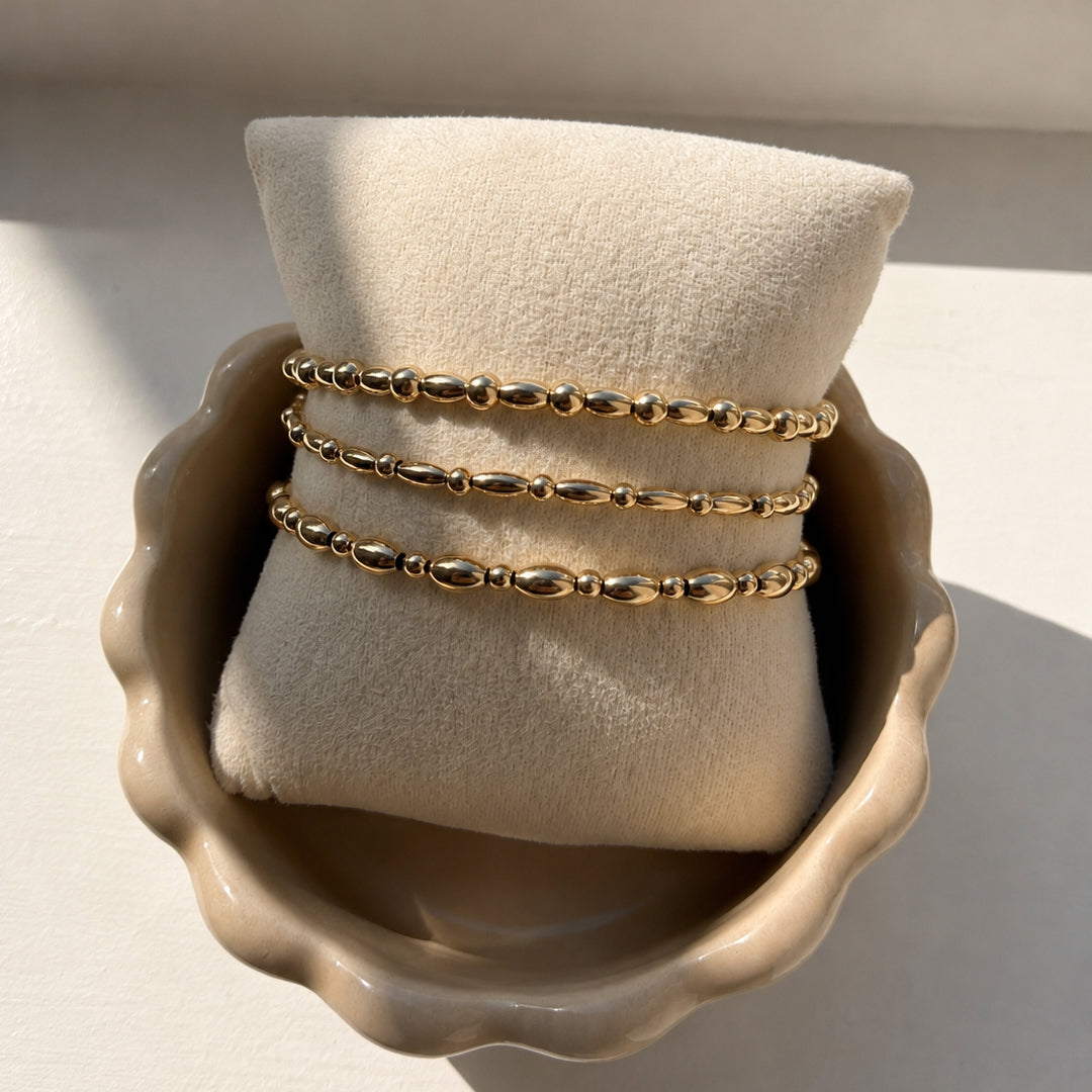 Drie gouden armbanden met ovale kralen en bolkralen van gold filled 14K op een sieradenkussen, van Bedels & Bedels.