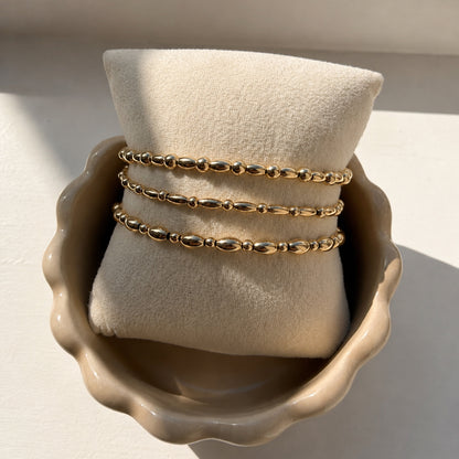 Drie gouden armbanden met ovale kralen en bolkralen van gold filled 14K op een sieradenkussen, van Bedels & Bedels.