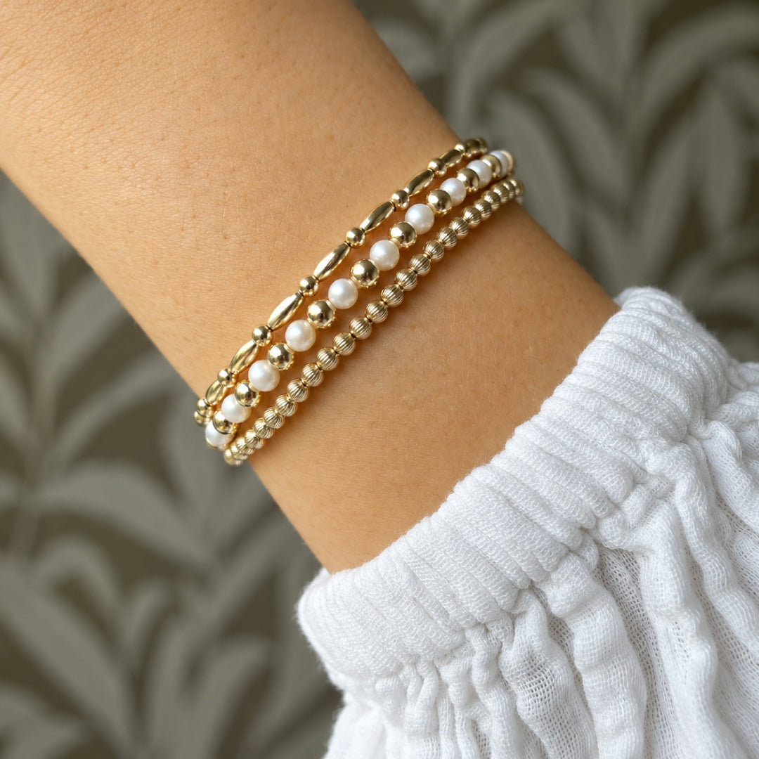 Pols met gestapelde gouden kralenarmbanden en parelarmbanden van gold filled 14K, van Bedels & Bedels.