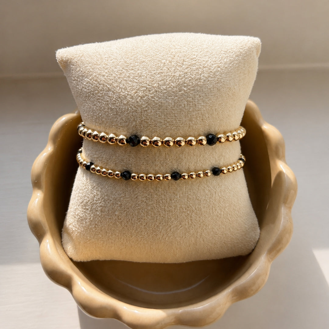 Armbanden met zwarte spinel en gouden kralen van gold filled 14K op een sieradenkussen, van Bedels & Bedels.