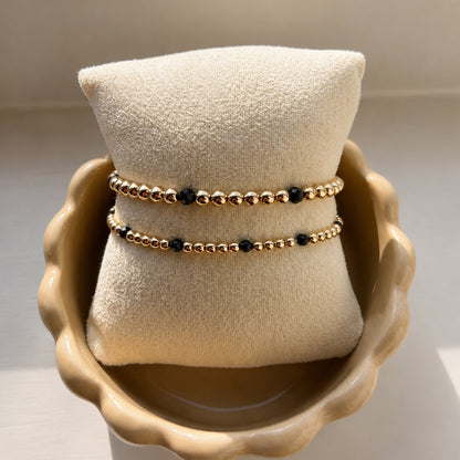 Armbanden met zwarte spinel en gouden kralen van gold filled 14K op een sieradenkussen, van Bedels & Bedels.